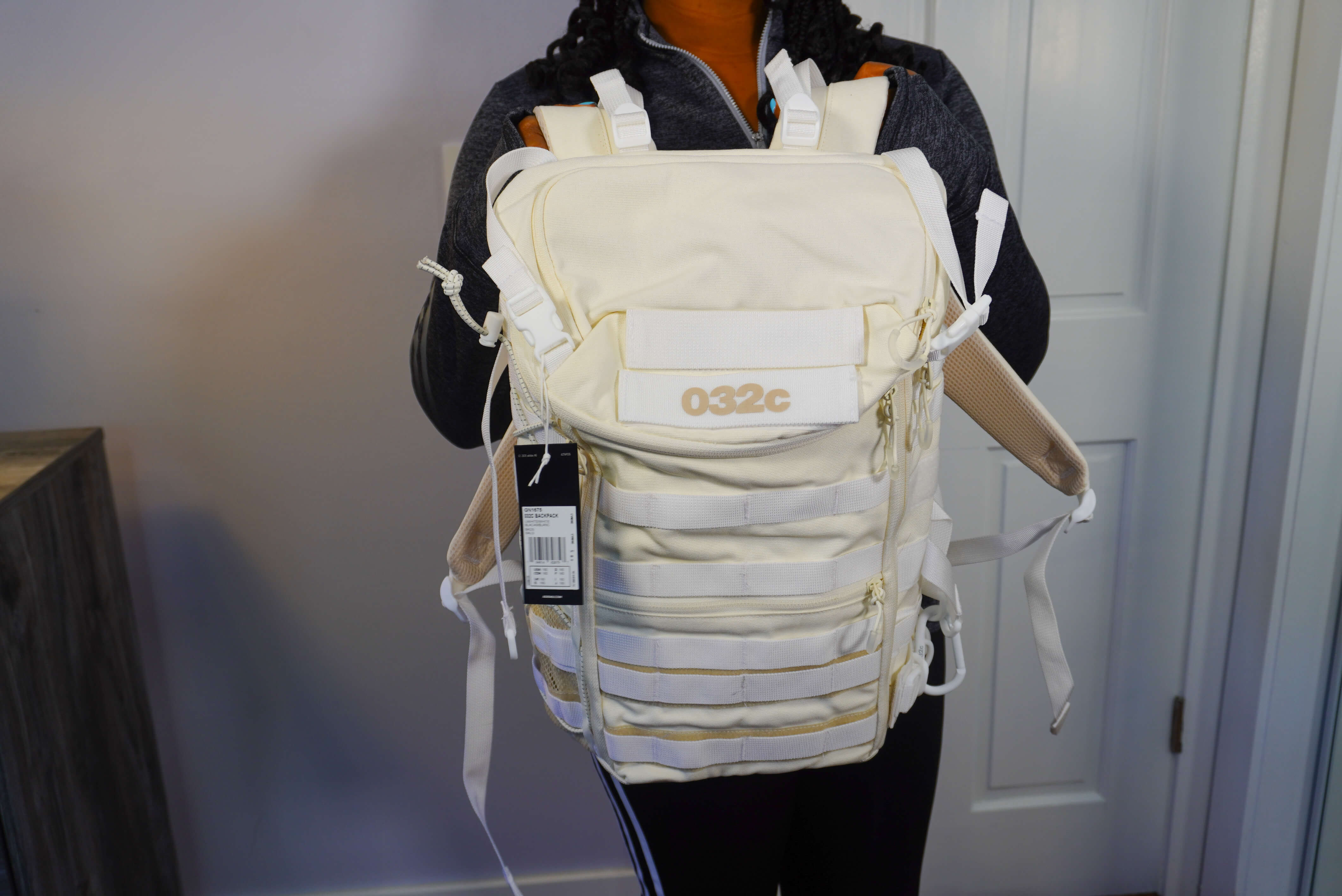 Image of me holding the Adidas X 032c backpack. The backpack is a cream color with white straps. On the front it says 032c and has hooks on the side.
