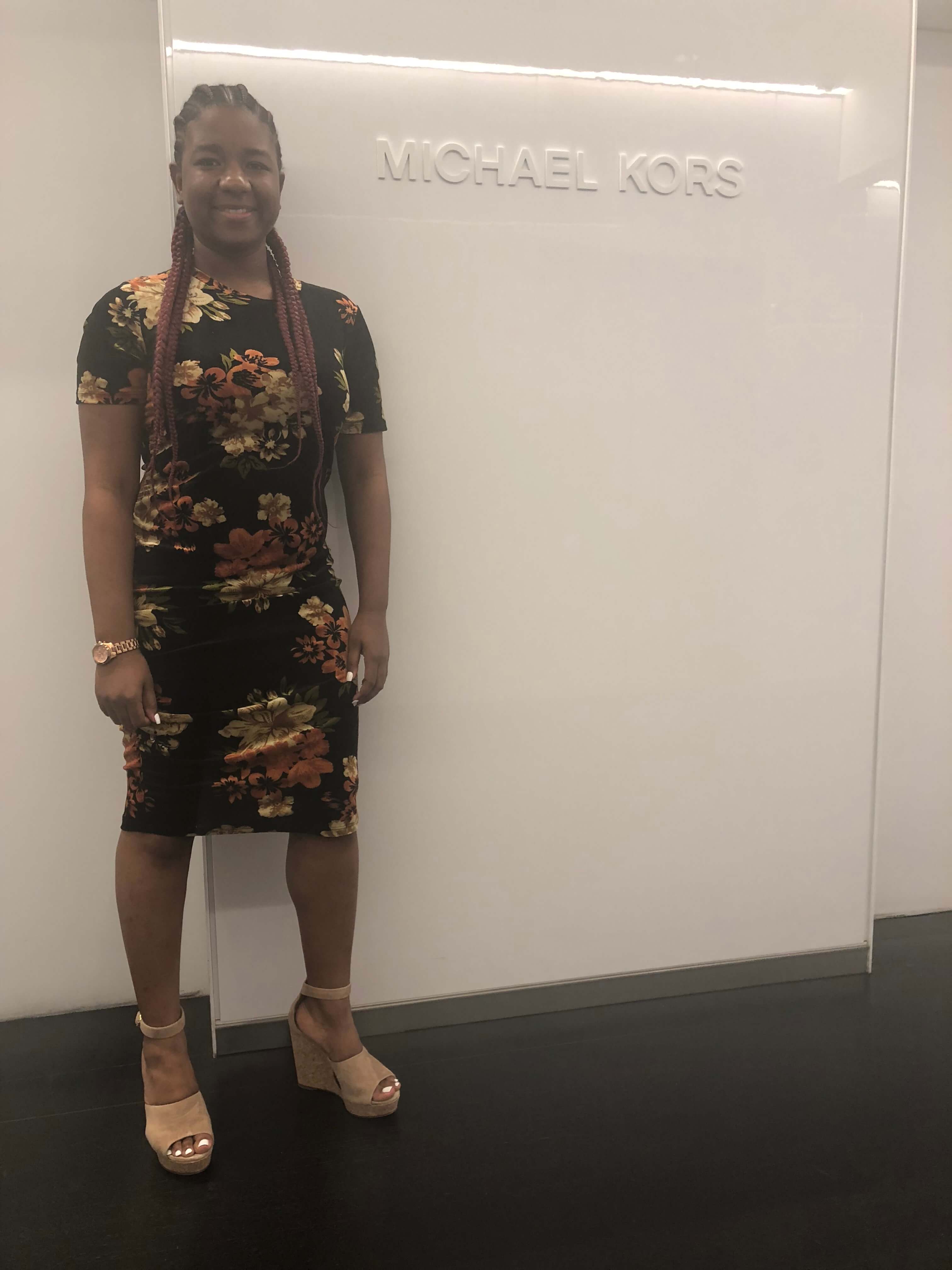 Picture of me at Michael Kors HQ wearing an all black dress with yellow and orange flowers.