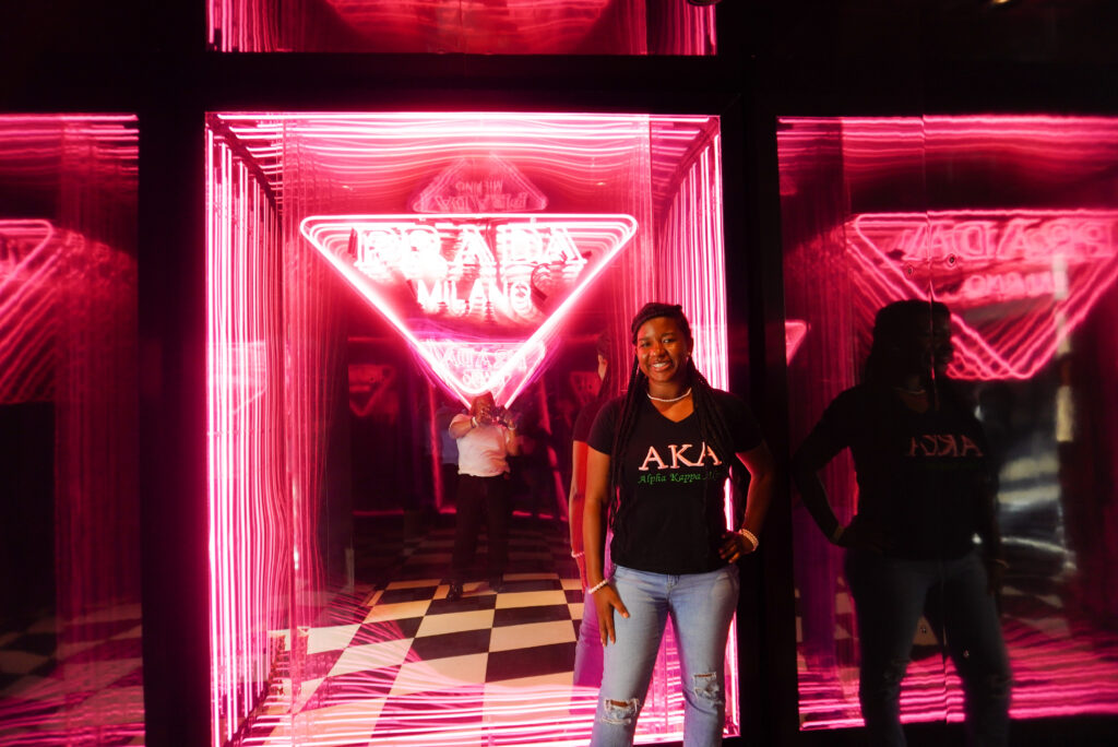 Image of me standing in front of neon Prada sign at pop-up event.