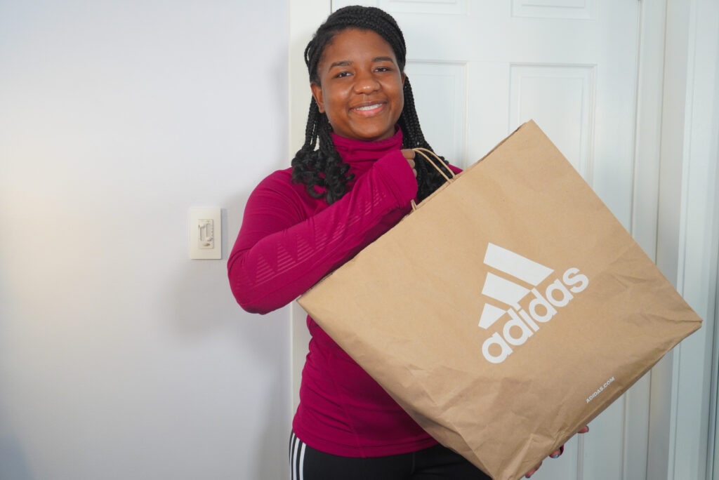 Image of me holding Adidas bag with different Adidas styles inside the shopping bag.