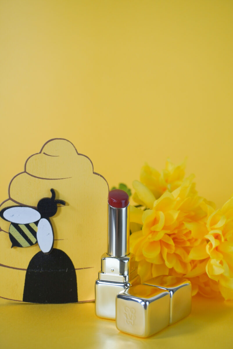 Image of Guerlain lipstick with a bee hive and yellow flowers in the background