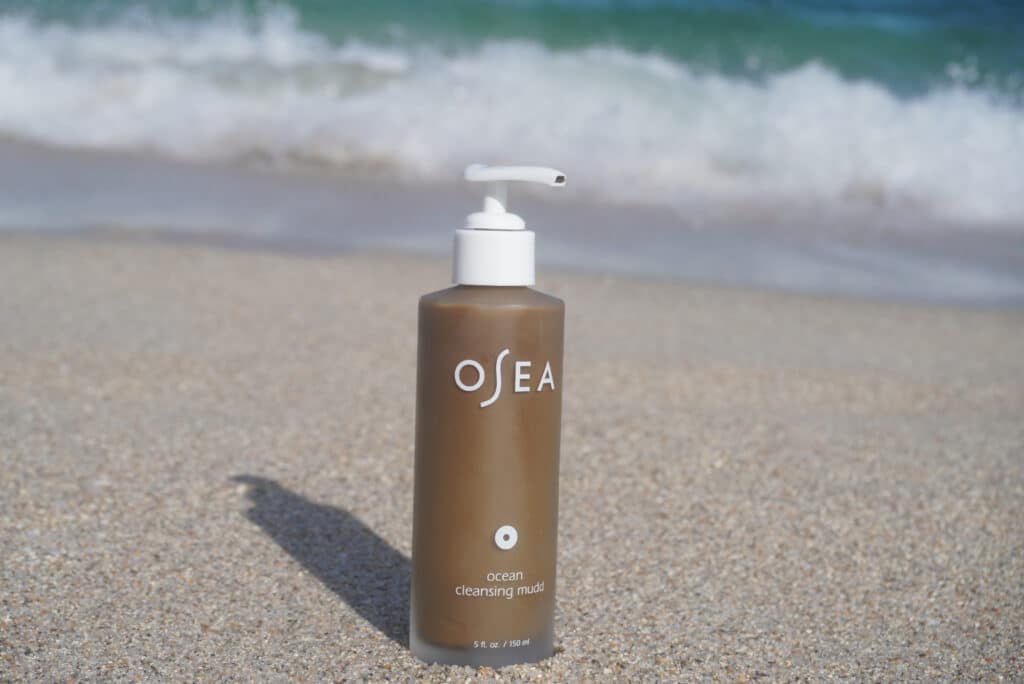 Image of the OSEA Ocean Mudd Cleanser sitting on the beach sand.